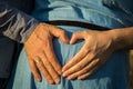 Close up, macro. Male and female hands carefully hold the stomach of a pregnant woman, their fingers form a heart