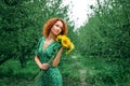 Close up, macro. The red-haired girl in a green vintage dress looks thoughtfully to the side, holding a bouquet of bright Royalty Free Stock Photo