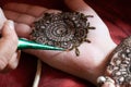 Close up macro shot of mehendi henna tattoo being applied in an intricate pattern on the hand of a woman with soft
