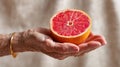 Close-up macro side view of a ruby red grapefruit half held by an elderly hand with textured skin and a golden bracelet Royalty Free Stock Photo