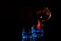 Close up, macro. Two glasses of alcohol, a hand with a match sets fire to the surface of one of the drinks. Black background. Royalty Free Stock Photo