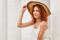 Close up, macro. Well-groomed red-haired curly girl poses near the white columns. She smiles and looks confidently at the camera.