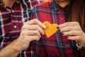 Close up, macro. Young lovers in red casual shirts hold a yellow heart carved from autumn leaf