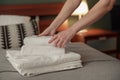 Close-up of maid hands putting stack of fresh white bath towels on bed sheet. Room service concept