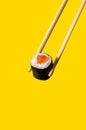 Close up Maki Roll with salmon fish on chopsticks on yellow background Royalty Free Stock Photo