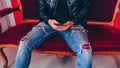 Young man resting with smartphone on small red sofa. Close-up of male body part sitting on armchair with mobile phone in Royalty Free Stock Photo