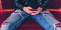 Young man resting with smartphone on small red sofa. Close-up of male body part sitting on armchair with mobile phone in Royalty Free Stock Photo