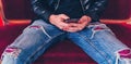 Young man resting with smartphone on small red sofa. Close-up of male body part sitting on armchair with mobile phone in