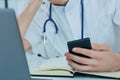 Close up male doctor or medical student using mobile smart phone working on laptop computer in hospital. Royalty Free Stock Photo