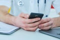 Close up male doctor or medical student using mobile smart phone working on laptop computer in hospital. Royalty Free Stock Photo