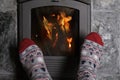 Close up of male feet legs in colored woolen socks are warming near flame, firewood burns in stove, fireplace, cozy winter evening Royalty Free Stock Photo