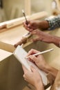 Close Up Of Male And Female Apprentices Working As Carpenters In Furniture Workshop Measuring Wood