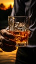 A close up of a male hand elegantly gripping a glass of whiskey