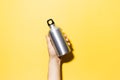Close-up of male hand holding aluminium eco water bottle isolated on yellow background.