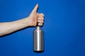 Close-up of male hand holding aluminum water bottle, showing thumbs up, on background of phantom blue color. Royalty Free Stock Photo