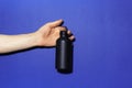 Close-up of male hand holding black reusable aluminum thermo water bottle on background of phantom blue color with copy space. Royalty Free Stock Photo