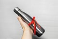 Close-up of male hand holding a eco water thermo bottle of steel with red ribbon, ecologic gift for any events. Isolated on white. Royalty Free Stock Photo
