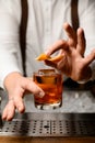 close-up of male hand holding glass with alcoholic drink and garnishing it with orange zest Royalty Free Stock Photo