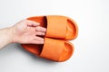 Close-up of male hand holding pair of orange slippers on white background.