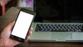 Close up male hand holding phone white screen over background of laptop, on wooden background. Royalty Free Stock Photo