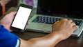 Close up male hand holding phone white screen over background of laptop, on wooden background. Royalty Free Stock Photo