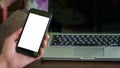 Close up male hand holding phone white screen over background of laptop, on wooden background. Royalty Free Stock Photo