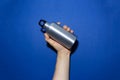 Close-up of male hand holding reusable, aluminum thermo bottle for water, on studio background of phantom blue color. Zero waste. Royalty Free Stock Photo