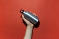 Close-up of male hand holding reusable, aluminum thermo bottle for water, on studio background of red color. Zero waste. Royalty Free Stock Photo