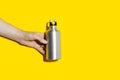 Close-up of male hand holding reusable, aluminum thermo bottle for water, on studio background of yellow color with copy space. Royalty Free Stock Photo