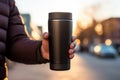 Close-up of male hand holding reusable steel black thermos water bottle on background of blurry road