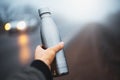 Close-up of male hand holding reusable steel thermo water bottle on background of foggy road. Royalty Free Stock Photo