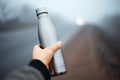 Close-up of male hand holding reusable steel thermo water bottle on blurred perspective outdoors background. Royalty Free Stock Photo