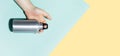 Close-up of male hand holding reusable thermo bottle. Backgrounds of pastel blue and yellow colors. Panoramic photo with space. Royalty Free Stock Photo