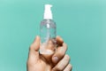 Close-up of male hand holding small plastic bottle of sanitizer antibacterial gel on background of cyan aqua menthe color.