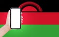 Close-up of male hand holding smartphone with blank on screen, on background of blurred flag of Malawi