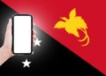 Close-up of male hand holding smartphone with blank on screen, on background of blurred flag of Papua New Guinea.