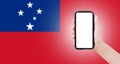 Close-up of male hand holding smartphone with blank on screen, on background of blurred flag of Samoa