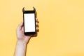 Close-up of male hand holding smartphone with devil horns and empty white mockup, isolated on yellow background. Royalty Free Stock Photo