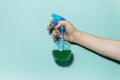 Close-up of male hand holding spray bottle for cleaning with blue pump, on cyan background. Royalty Free Stock Photo