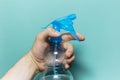 Close-up of male hand holding spray bottle for cleaning with blue pump, on cyan background.