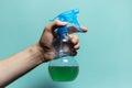 Close-up of male hand holding spray bottle for cleaning with blue pump, on cyan background. Royalty Free Stock Photo