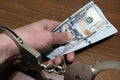 Close-up of a male hand holding a stack of US dollars with handcuffs on a brown background. The concept of violation of the law in Royalty Free Stock Photo