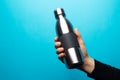 Close-up of male hand holding steel reusable thermo water bottle with focus on cap, against background of blue color. Royalty Free Stock Photo