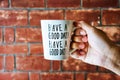 Close up of male hand holding white coffee or tea cup with text `HAVE A GOOD DAY!` on old red brick wall background