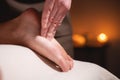 Close-up male hand of masseur doing massage of feet of female client in a dark room of saved salon by candlelight