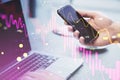 Close up of male hand using laptop and cellphone with falling candlestick forex chart and index on blurry background. Crisis and