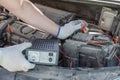 Close-up of male hands checking voltage of automobile battery under hood machine with accuracy. Automotive checkup concept