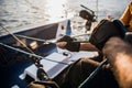 Close-up of male hands in gloves pulling rope of sailboat while mooring yacht and sitting with friends on deck.