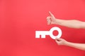 Close up of male hands holding big white key and showing thumb up, excellent symbol, isolated over red color background wall in Royalty Free Stock Photo