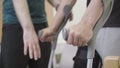 Close-up of male hands holding crutches start walking in hospital ward. Unrecognizable nurse doctor or volunteer helping